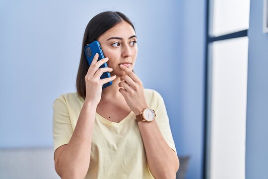 Young hispanic woman with serious expression talking on the smartphone at home