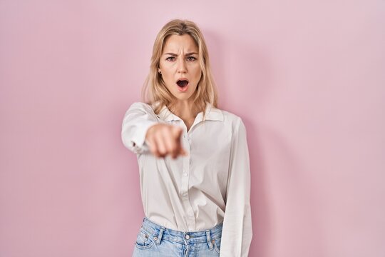 Young caucasian woman wearing casual white shirt over pink background pointing displeased and frustrated to the camera, angry and furious with you