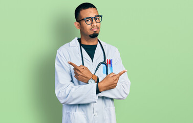 Young african american man wearing doctor uniform and stethoscope pointing to both sides with fingers, different direction disagree - Powered by Adobe