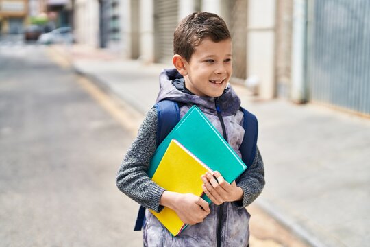 Blond child student holding books standing at street