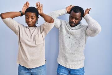 Young african american couple standing over blue background together doing bunny ears gesture with...