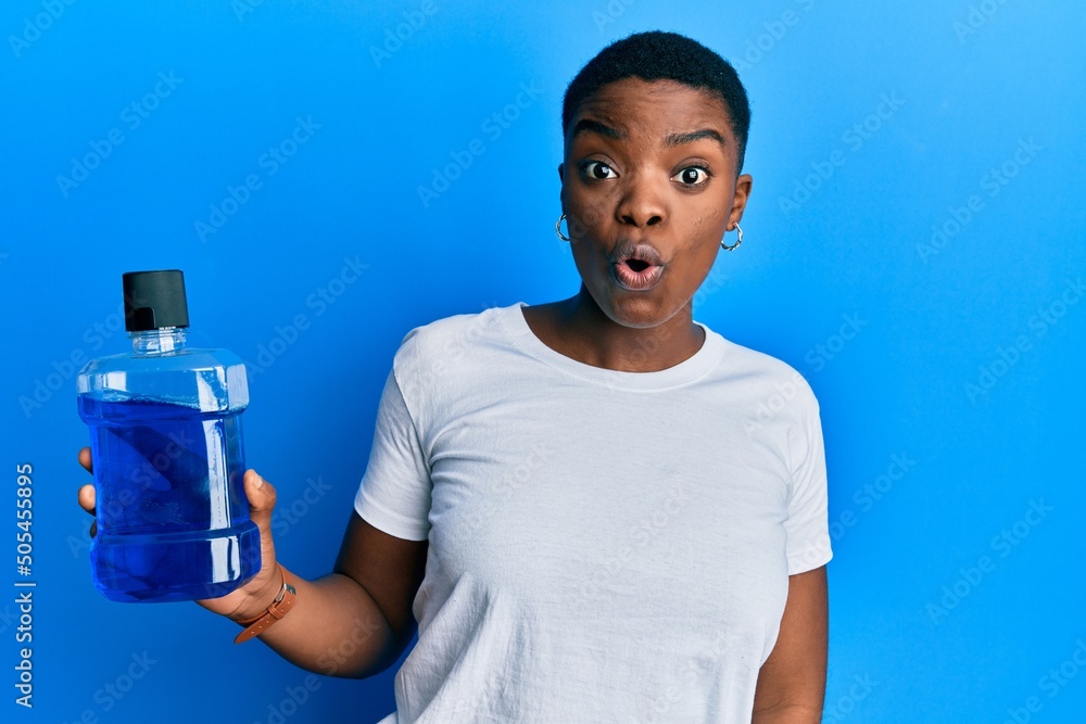 Sticker young african american woman holding mouthwash for fresh breath scared and amazed with open mouth fo