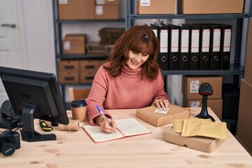 Fototapeta na wymiar Middle age woman ecommerce business worker writing on book at office