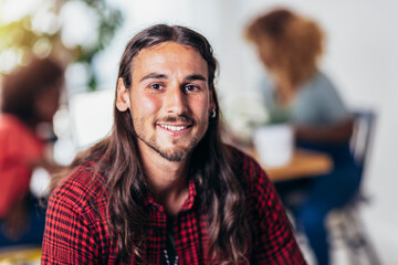 Young handsome man with long hair smiling and looking at camera with friends in background.