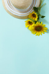Straw hat and sunflowers on green background. Summer holiday, vacation concept. Flat lay, top view, copy space.