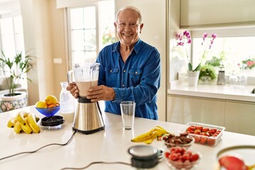 Senior man smiling confident holding jar of smoothie at kitchen