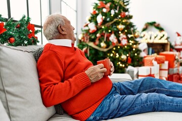 Obraz na płótnie Canvas Senior grey-haired man drinking coffee celebrating christmas sitting on the sofa at home.