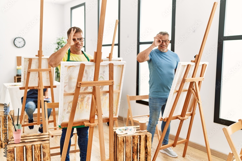 Poster group of middle age people artist at art studio smiling happy doing ok sign with hand on eye looking