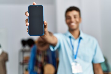 Young hispanic man working as shop assistant showing phone screen at retail shop