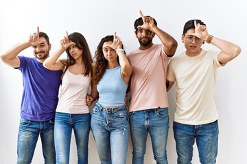 Group of young people standing together over isolated background making fun of people with fingers on forehead doing loser gesture mocking and insulting.