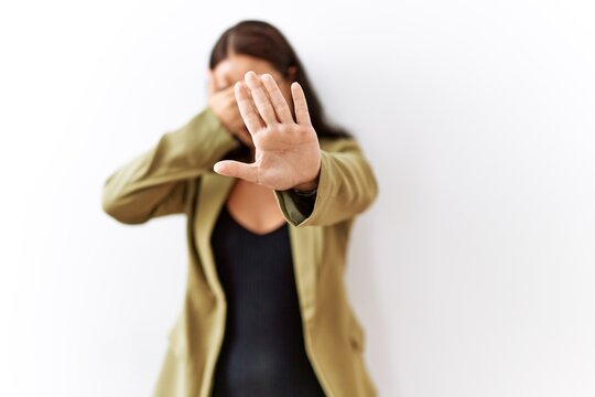Young brunette woman standing over isolated background covering eyes with hands and doing stop gesture with sad and fear expression. embarrassed and negative concept.
