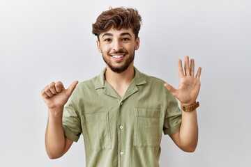 Young arab doctor man standing over isolated background showing and pointing up with fingers number six while smiling confident and happy.