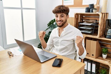 Young arab man working using computer laptop at the office screaming proud, celebrating victory and success very excited with raised arms