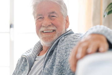 Portrait of happy bearded senior man relaxing on sofa at home looking at camera smiling. Headshot of elderly attractive man enjoying retirement.