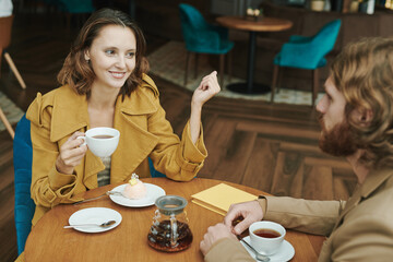 Portrait of serious modern guy with beard sitting at round table in loft cafe and calling by mobile phone