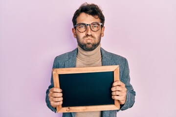 Handsome man with beard holding blackboard puffing cheeks with funny face. mouth inflated with air, catching air.