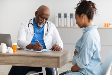 Male doctor consulting young smiling pregnant woman, writing record - obrazy, fototapety, plakaty