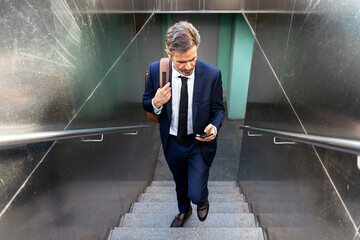 Businessman walking upstairs and using smartphone