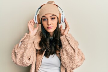 Young hispanic woman listening to music using headphones relaxed with serious expression on face. simple and natural looking at the camera.