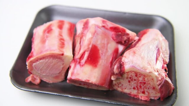 Macro closeup rack focus of beef marrow bones in package container with red uncooked raw meat isolated against white background table
