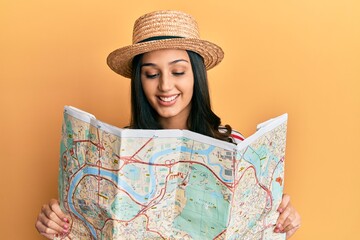 Young hispanic woman wearing summer hat holding map smiling with a happy and cool smile on face....