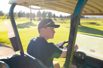 Rear view of caucasian young man wearing cap looking away while driving golf cart in summer