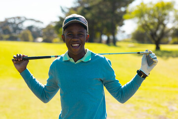 Portrait of smiling african american young man wearing cap holding golf club standing at golf course
