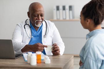Experienced black doctor showing pills to female patient - obrazy, fototapety, plakaty