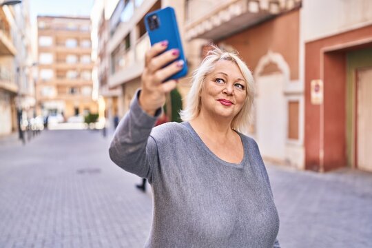 Middle age blonde woman smiling confident making selfie by the smartphone at street