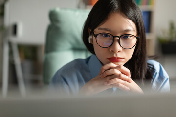 Asian woman using laptop at home office and thinking