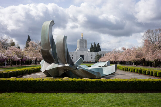 Salem, OR, USA - Mar 31, 2022: The Oregon State Capitol viewed from the Capitol Fountain, an outdoor cast bronze fountain and sculpture, on a beautiful spring day during cherry blossom season.