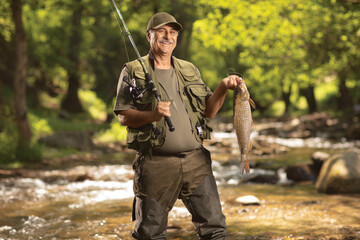 Naklejka premium Smiling mature fisherman holding a carp fish and standing in a river