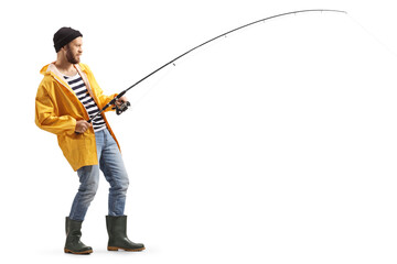 Full length profile shot of a young man in a raincoat and boots fishing with a rod