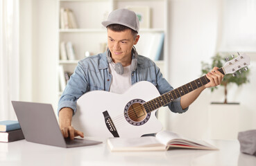 Young man with an acoustic guitar looking at a laptop computer