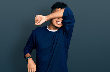 Young african american man wearing casual clothes covering eyes with arm smiling cheerful and funny. blind concept.