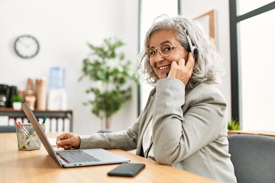 Middle age grey-haired call center agent woman smiling happy working at the office.