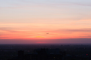 Airplane flying in beautiful sunset sky over the dusky cityscape