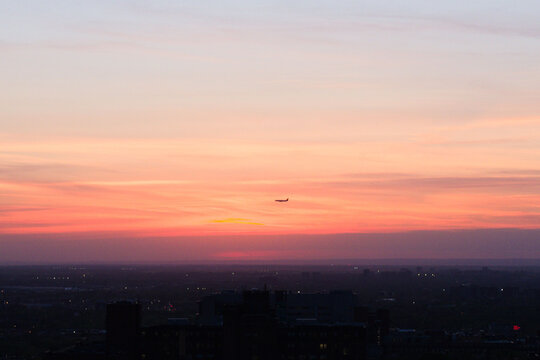 Airplane flying in beautiful sunset sky over the dusky cityscape