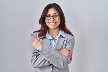 Hispanic young business woman wearing glasses with a big smile on face, pointing with hand and finger to the side looking at the camera.
