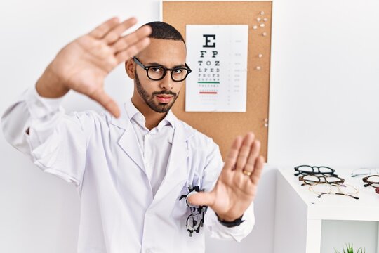 African american optician man standing by eyesight test doing frame using hands palms and fingers, camera perspective