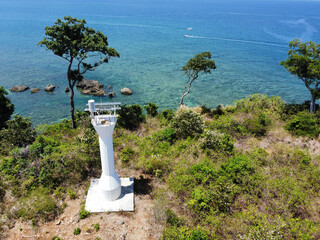 High angle of lighthouse on a mountain covered with greenery against a sea on a sunny day