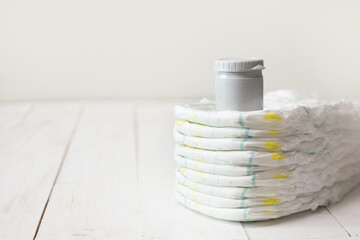 Stack of baby diapers with skin care cream on white wooden table