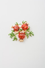 Metallic brooch in shape of three pomegranate fruits with green leaves, pin on white background, bijouterie, jewelry close up