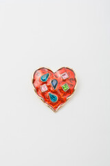 Metallic golden brooch in shape of red heart with bright gemstones imitation, pin on white background, bijouterie, jewelry close up