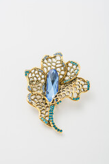 Metallic brooch in shape of flower with golden petals and blue gemstone imitation, pin isolated on white background, bijouterie, jewelry close up