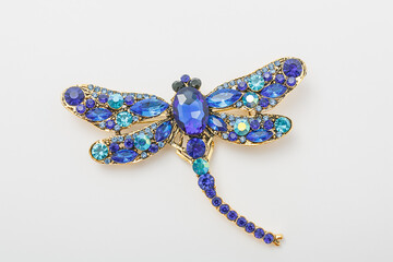 Metallic brooch in shape of dragonfly with blue gemstone imitation, pin isolated on white background, bijouterie, jewelry close up