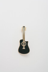Metallic golden brooch in shape of black guitar, pin on white background. Bijouterie, jewelry for musician, close up