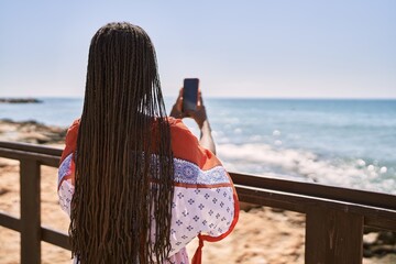 Young african american woman on back view make picture using smartphone at the beach. - Powered by Adobe