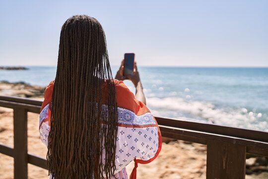 Young african american woman on back view make picture using smartphone at the beach.