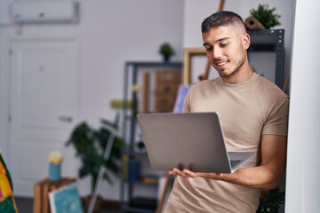 Young hispanic man artist smiling confident using laptop at art studio